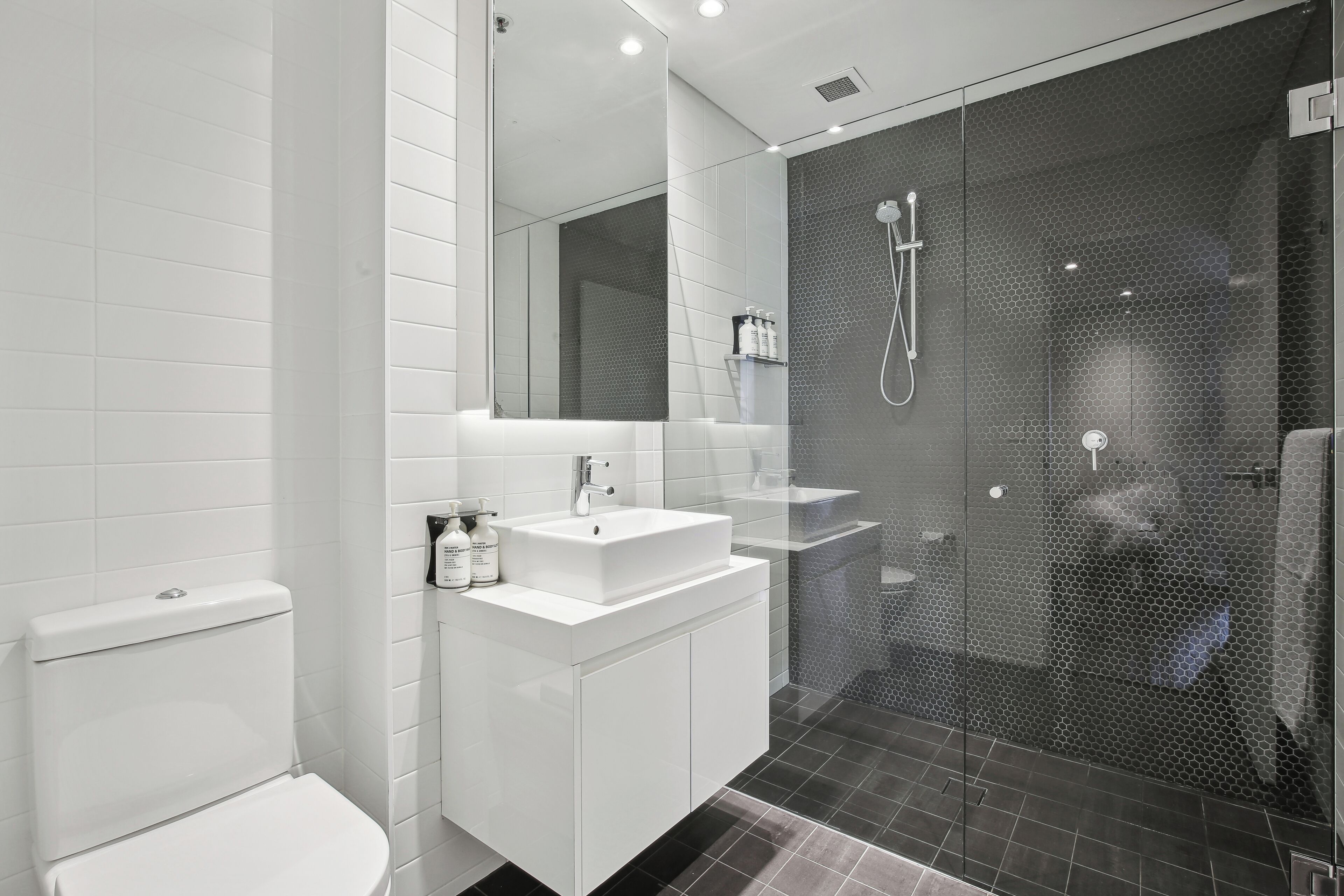 Une salle de bain moderne avec des toilettes, un lavabo blanc et une douche à parois de verre.