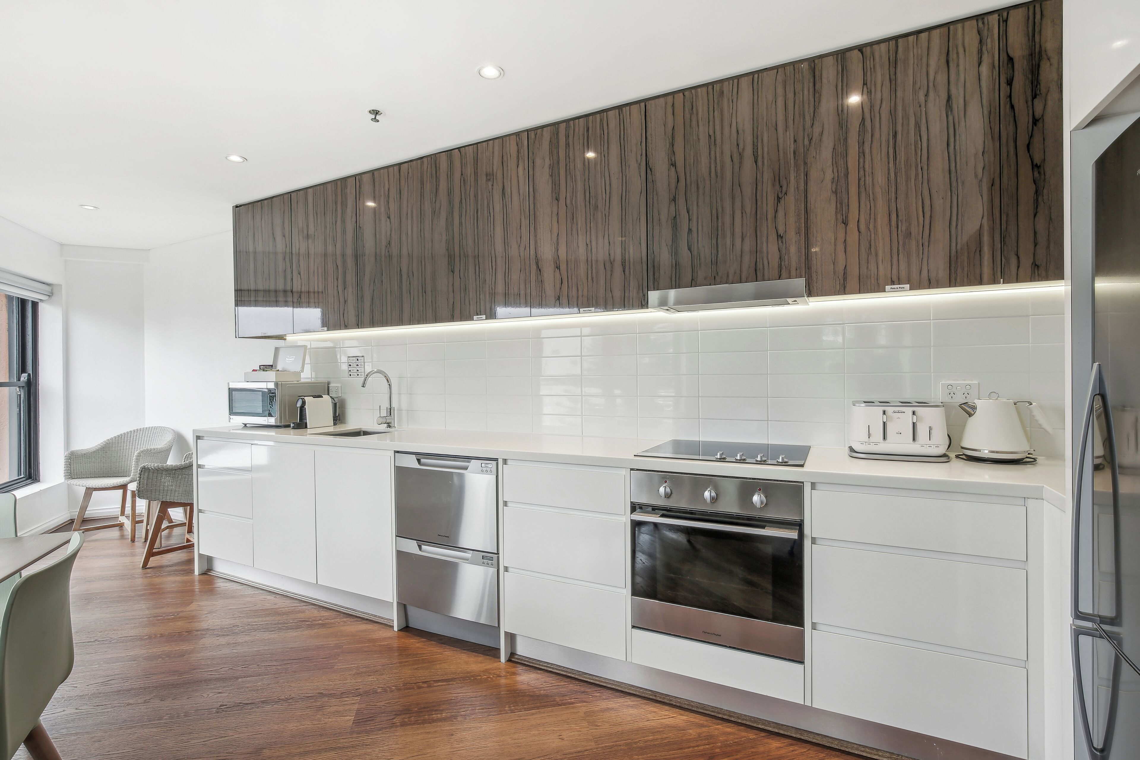 Una cocina moderna con armarios blancos, electrodomésticos de acero inoxidable y una pared decorativa de madera.