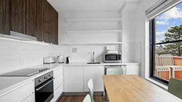 Una cocina moderna con armarios blancos, una mesa de comedor de madera y vistas a una zona de estar exterior a través de un amplio ventanal.