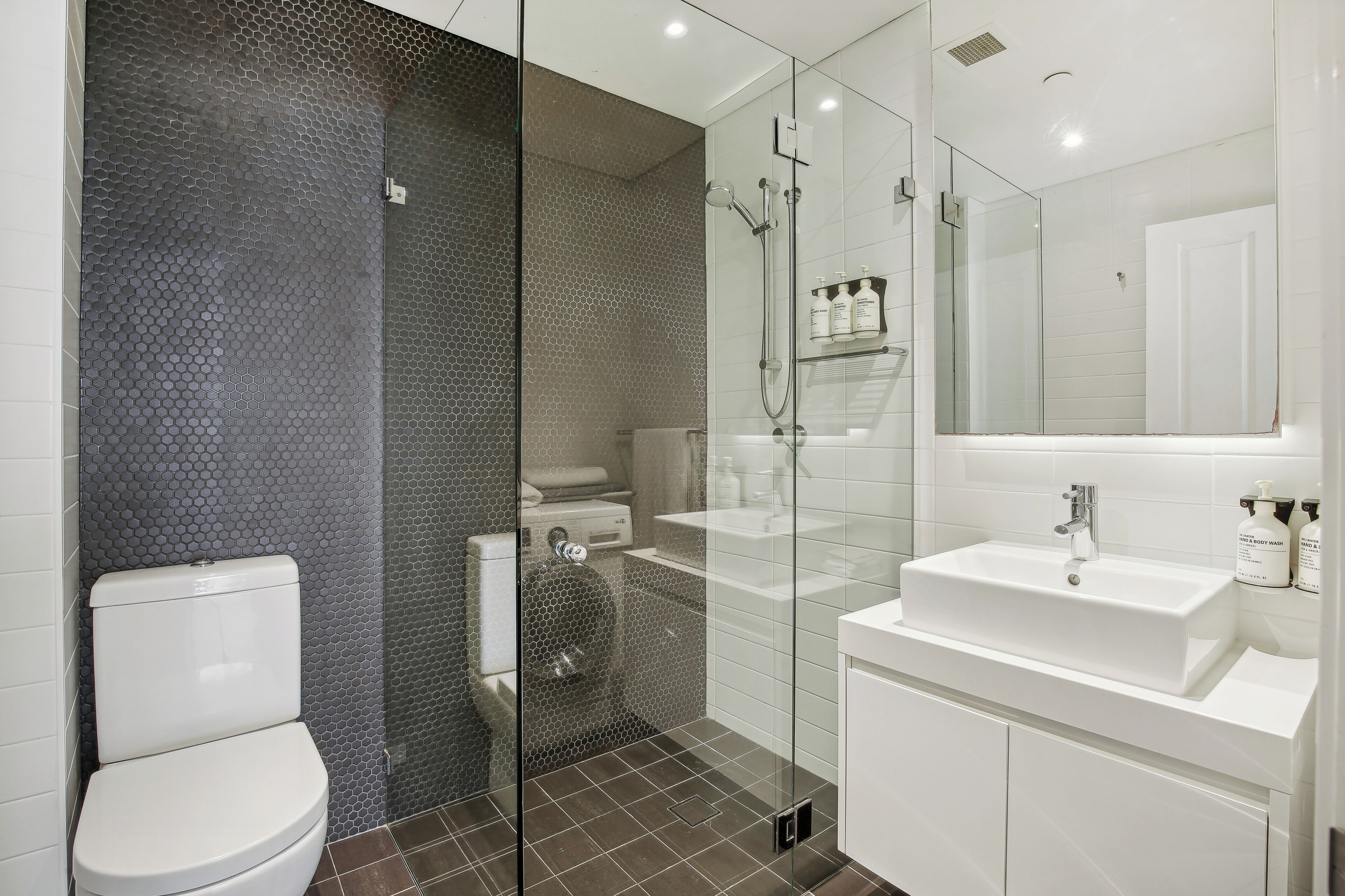 A modern bathroom with a glass-enclosed shower, a white sink, and a toilet.