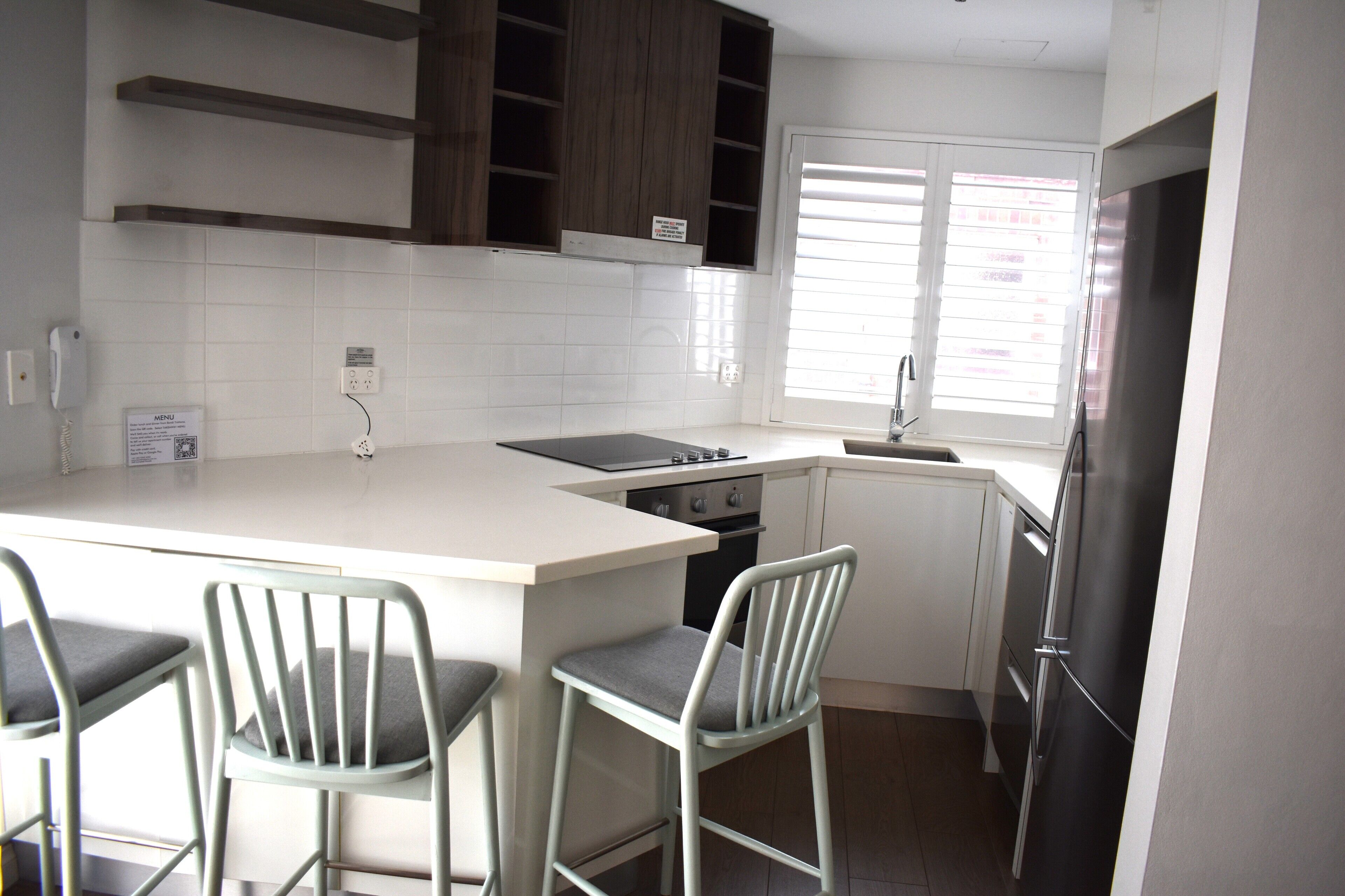 A compact kitchen with a central island, bar stools, a built-in oven, and a refrigerator.