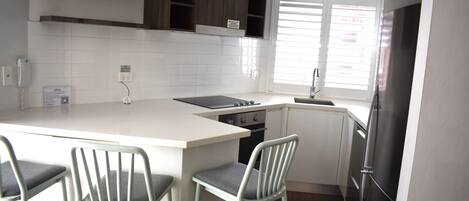 A compact kitchen with a central island, bar stools, a built-in oven, and a refrigerator.