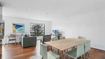 A modern living room with a wooden dining table, green chairs, a grey sofa, and a TV.