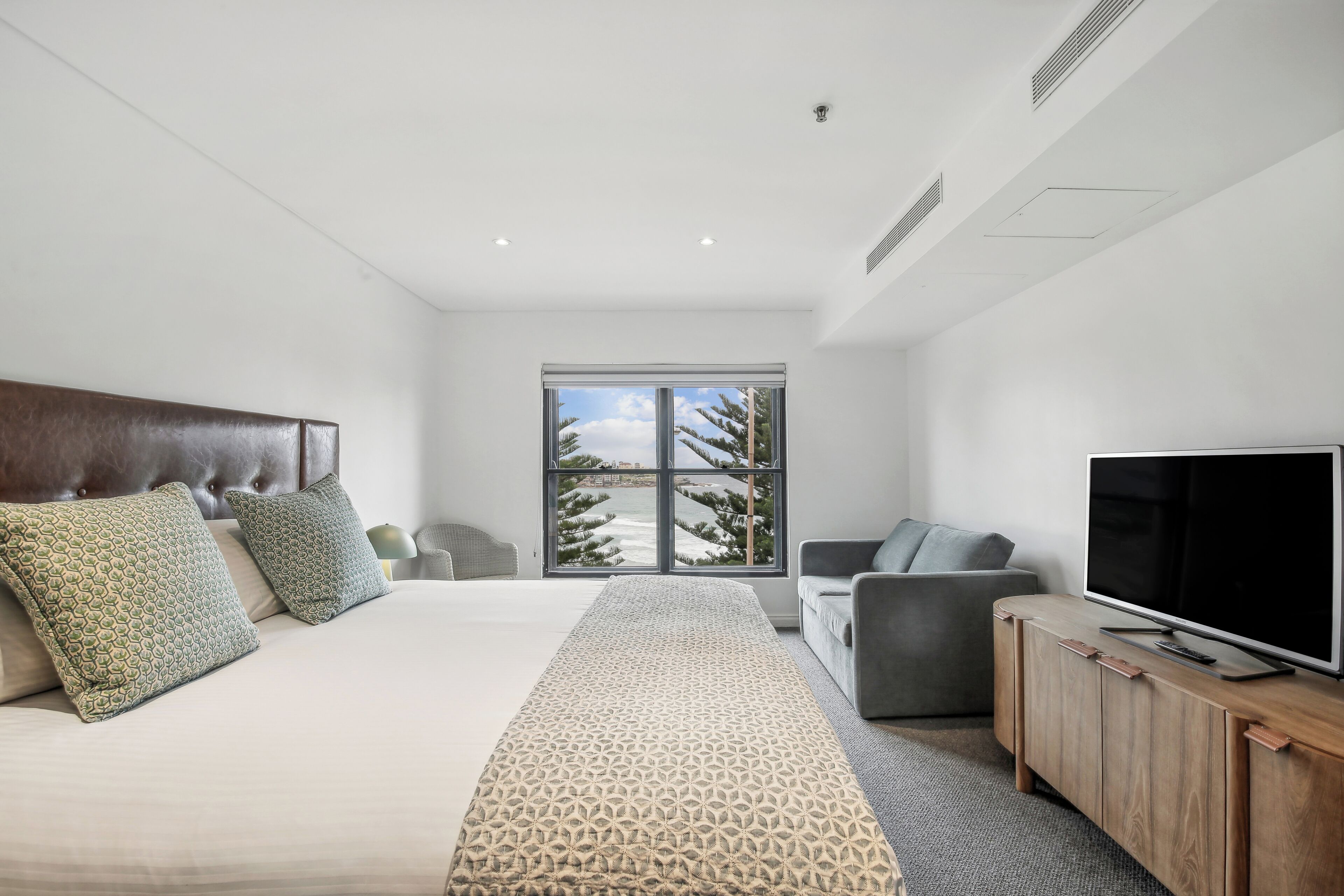 A modern bedroom with a large bed, a TV on a wooden cabinet, and a view of trees outside.
