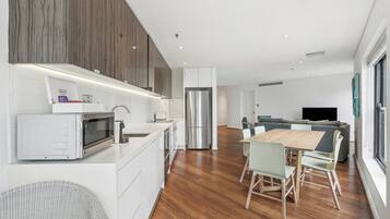 Una cocina moderna con armarios blancos, un refrigerador de acero inoxidable y una zona de comedor con mesa y sillas de madera.