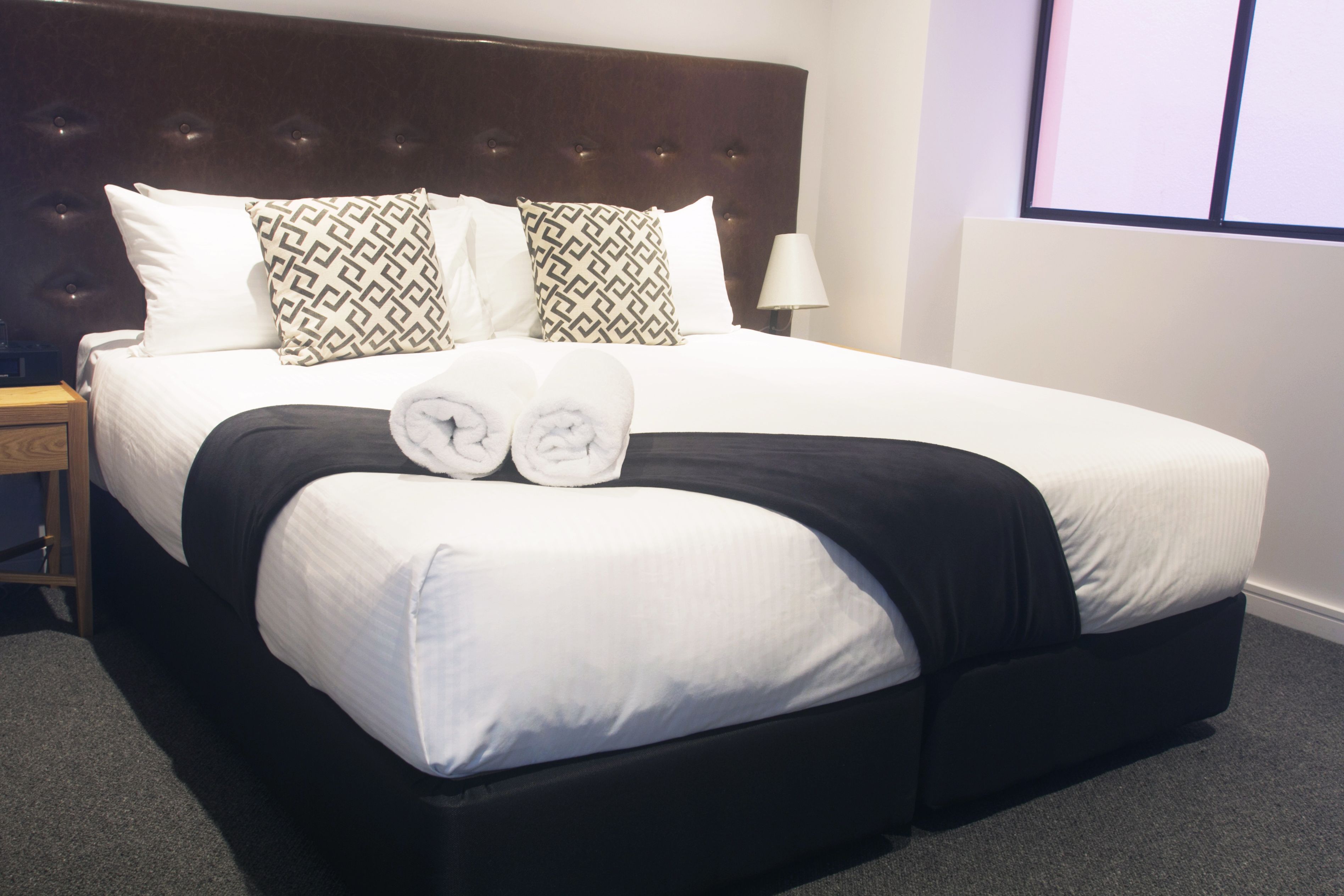 A neatly made bed with a dark headboard, white bedding, and patterned pillows.