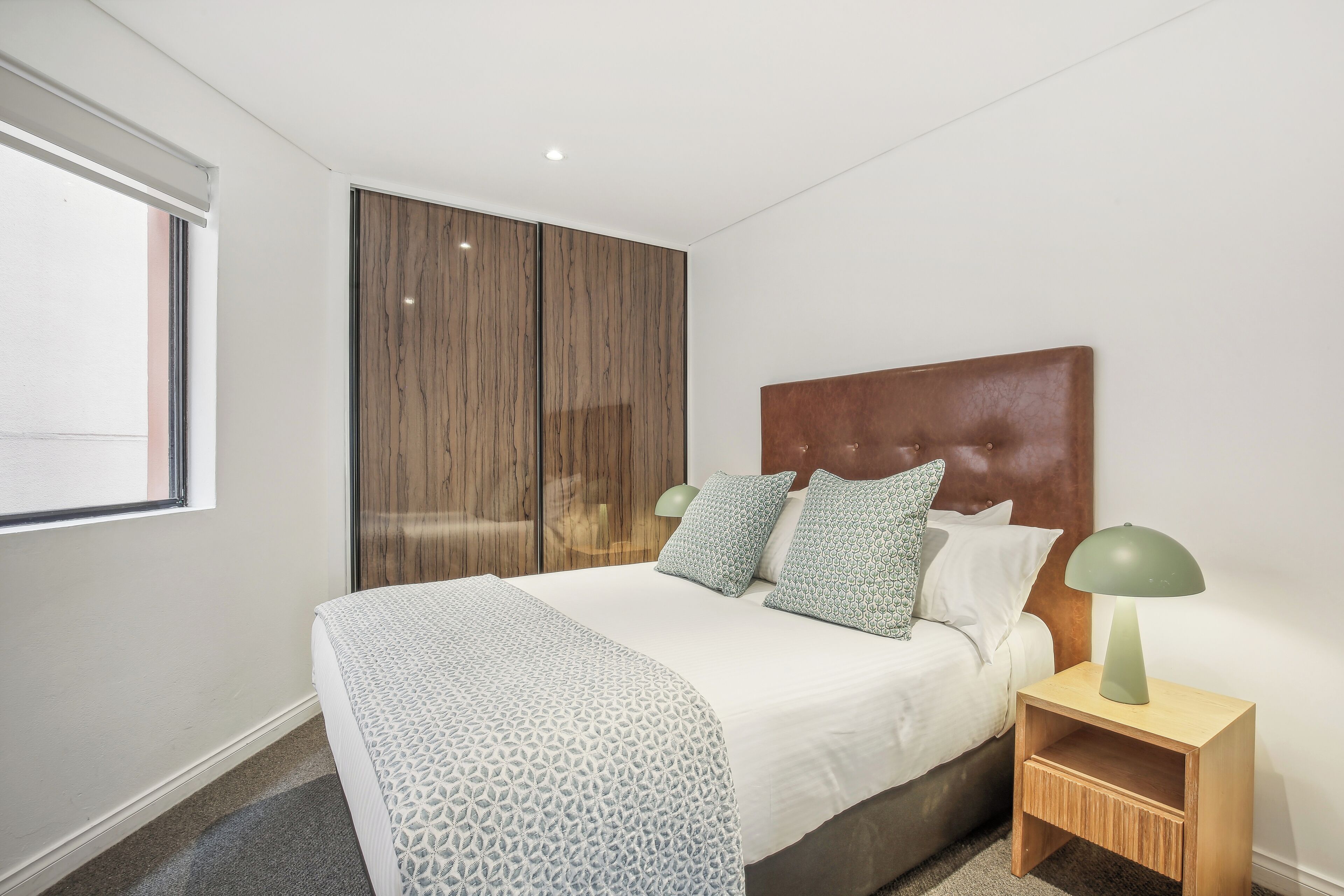 A modern bedroom with a large bed, a wooden wardrobe, and a nightstand with a lamp.
