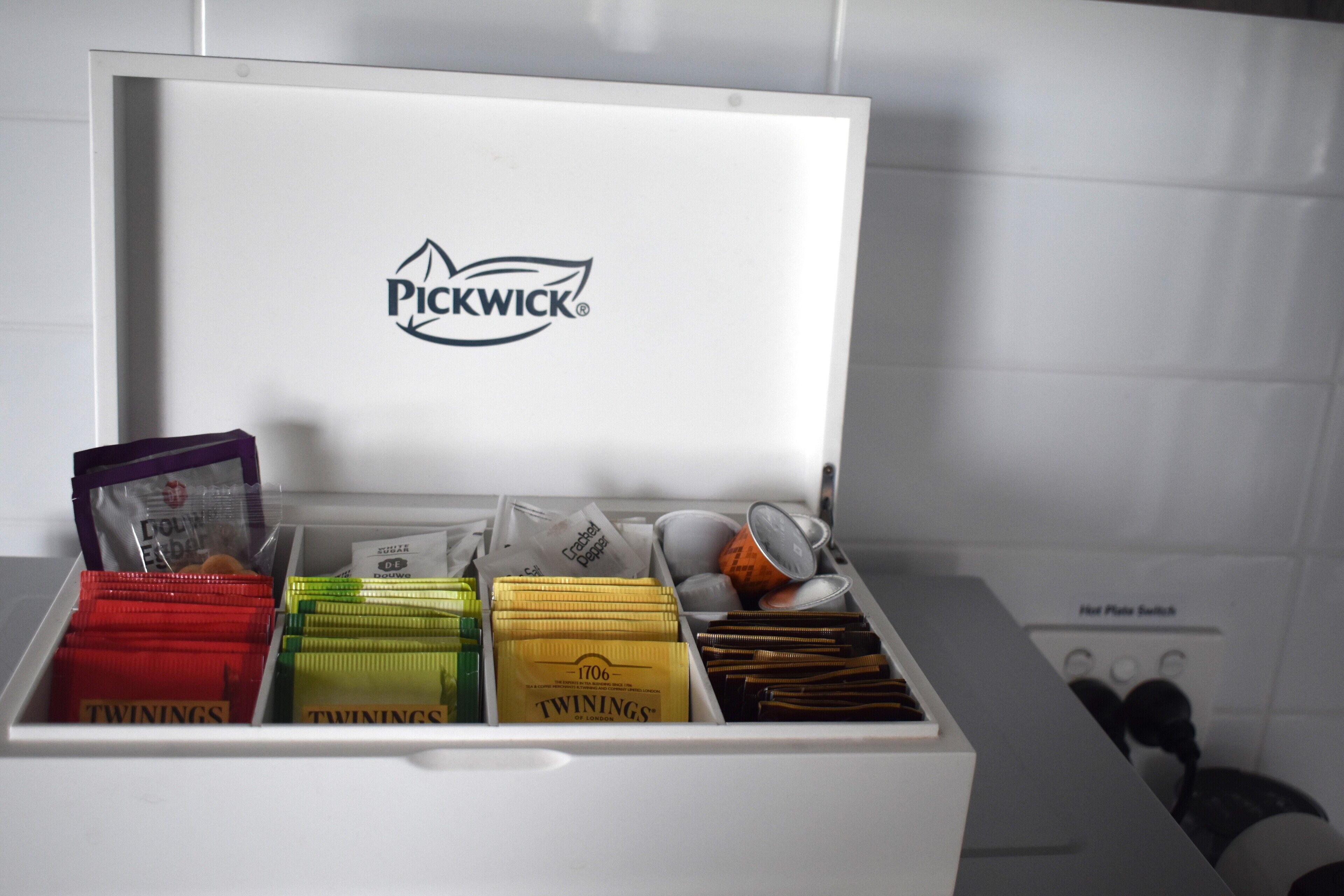 En hvid opbevaringskasse med rum, der indeholder forskellige genstande, inklusiv et tydeligt Pickwick logo på låget.