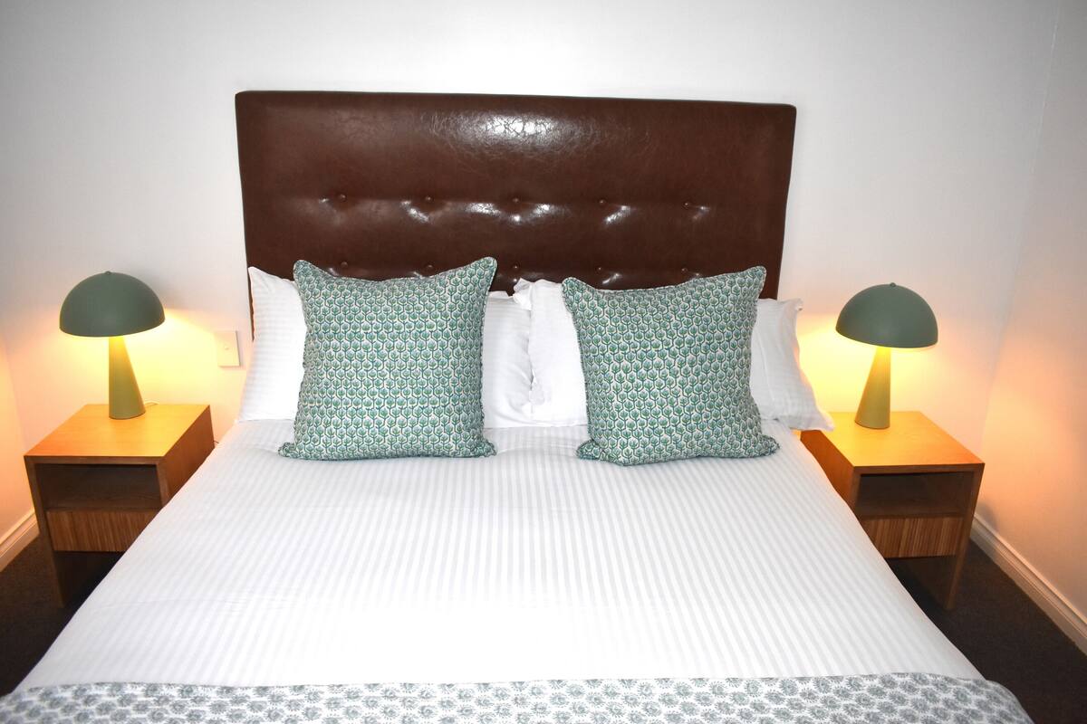 A neatly made bed with a tufted headboard, two matching pillows, and two bedside lamps on wooden nightstands.