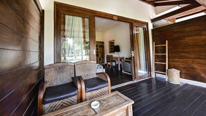 Habitación con suelo de madera, un sofá y una mesita, una puerta de madera y vistas a otra habitación con un televisor.