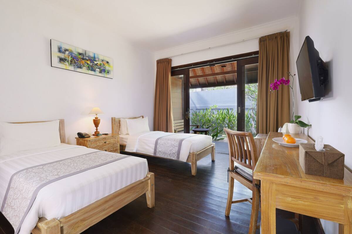 Ein Hotelzimmer mit zwei Betten, einem Holztisch, einem Fernseher und einem Balkon mit Blick.