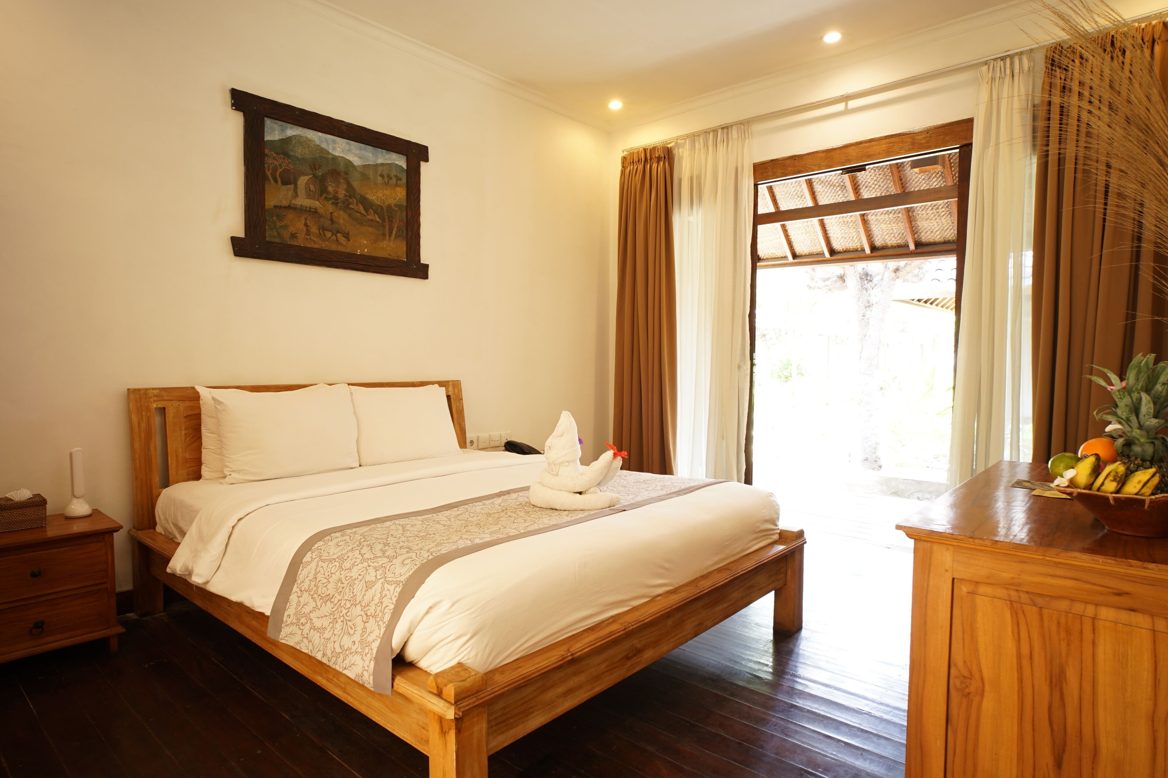 A wooden bed with white linens, a nightstand, a painting on the wall, and a fruit bowl on the dresser.
