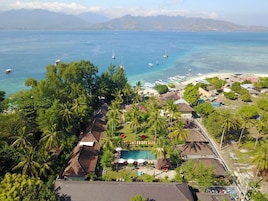 Un resort con piscina, palmeras y barcos al fondo.