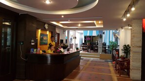 A hotel reception area with a reception desk, a clock, and a counter with informational brochures. - MT Hotel Patong (Patong)