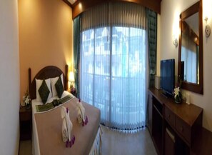 A hotel room with a bed, a TV, a desk, and a large window with curtains.