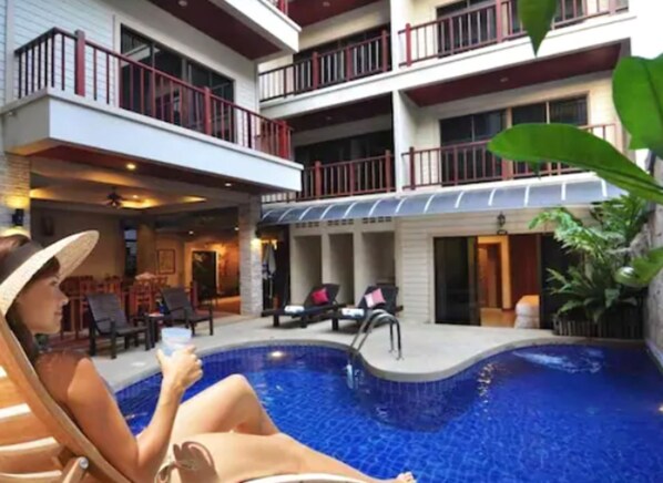 Una piscina al aire libre, sombrillas, sillones reclinables de piscina