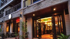 A hotel entrance with a brick facade, outdoor seating area, and potted plants. - MT Hotel Patong (Patong)