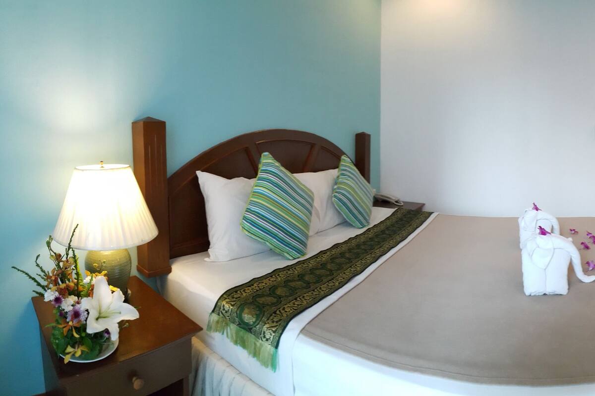 A hotel room with a bed, a nightstand with a lamp, a dresser, a TV, and a mirror.