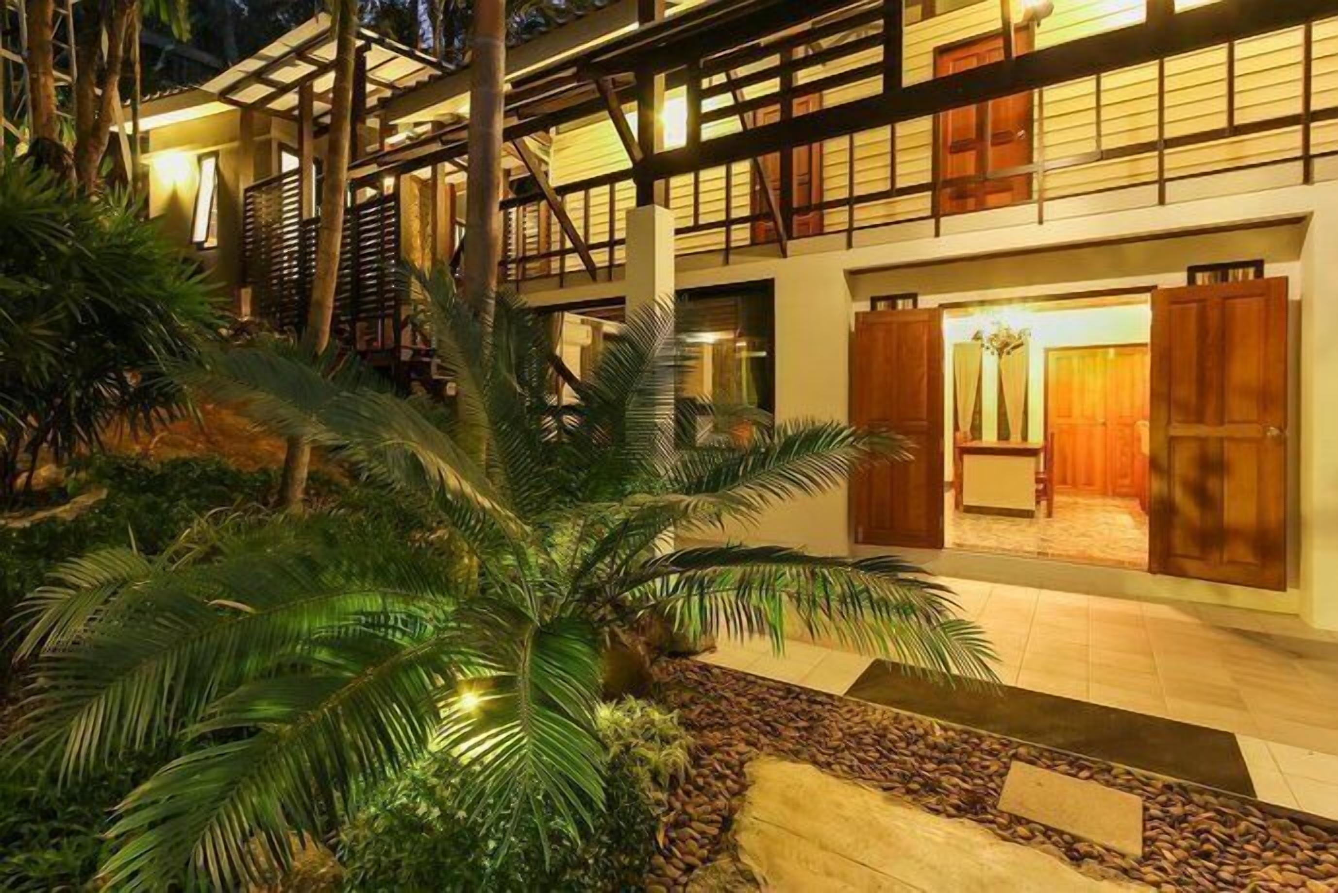 A hotel with a covered outdoor area, palm trees, and a tiled walkway.