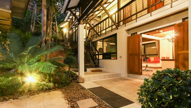 A modern house with a balcony, a staircase, and a well-lit interior. - Kata Tranquil Villa (Karon)