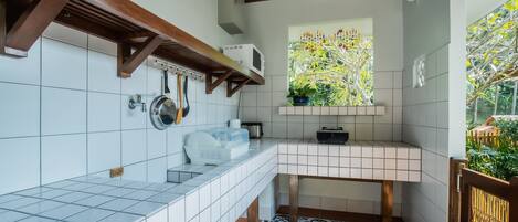 A kitchen with white tiles, a wooden ceiling, a window with a view of greenery, and a tiled floor with a black and white pattern.