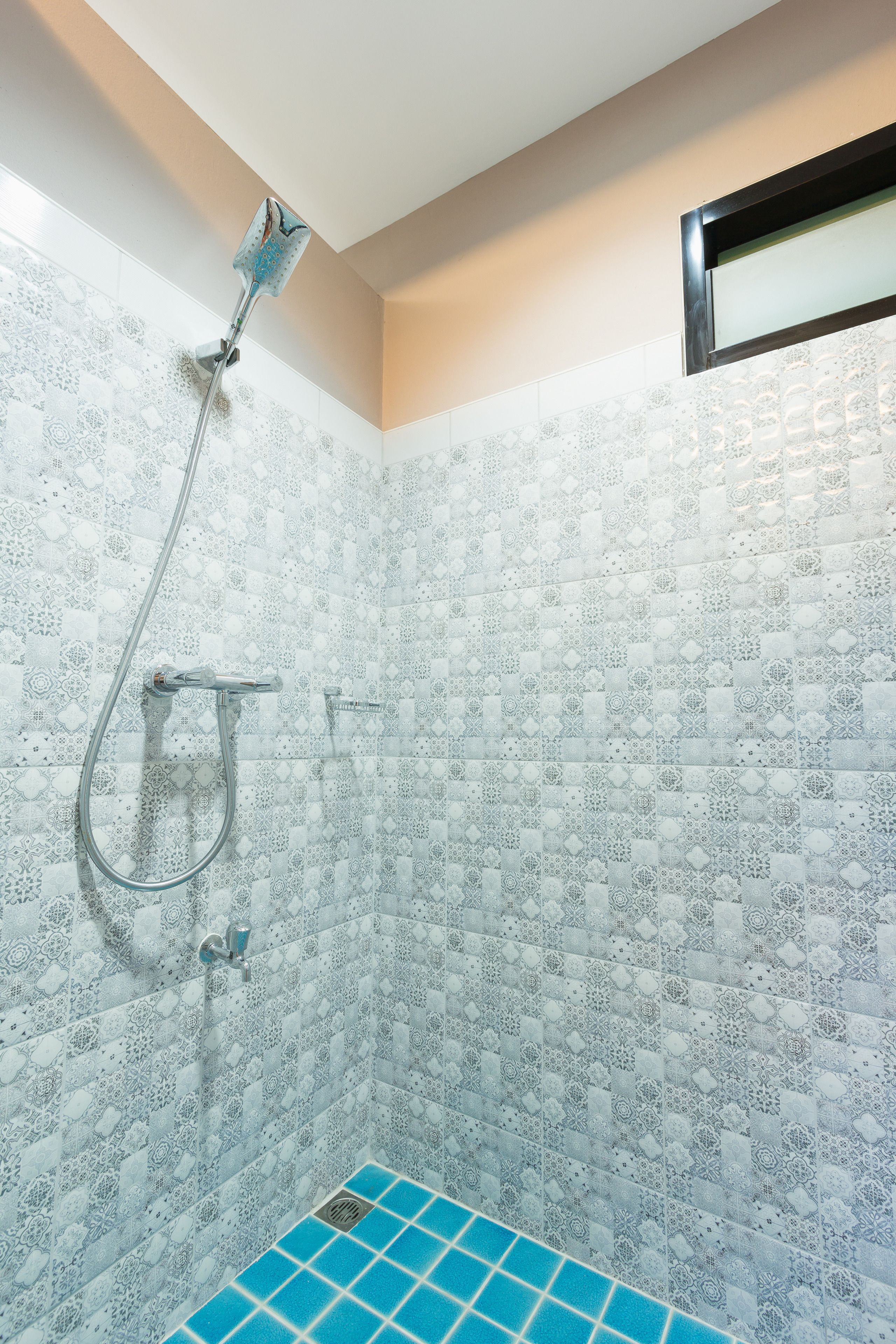 A shower with a patterned tile wall and a blue tiled floor.