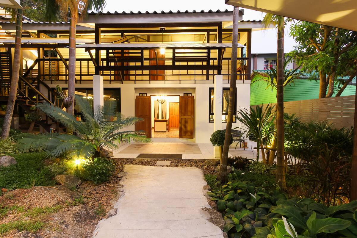 Un edificio de dos pisos con un área exterior cubierta, una escalera y un sendero que conduce a la entrada.