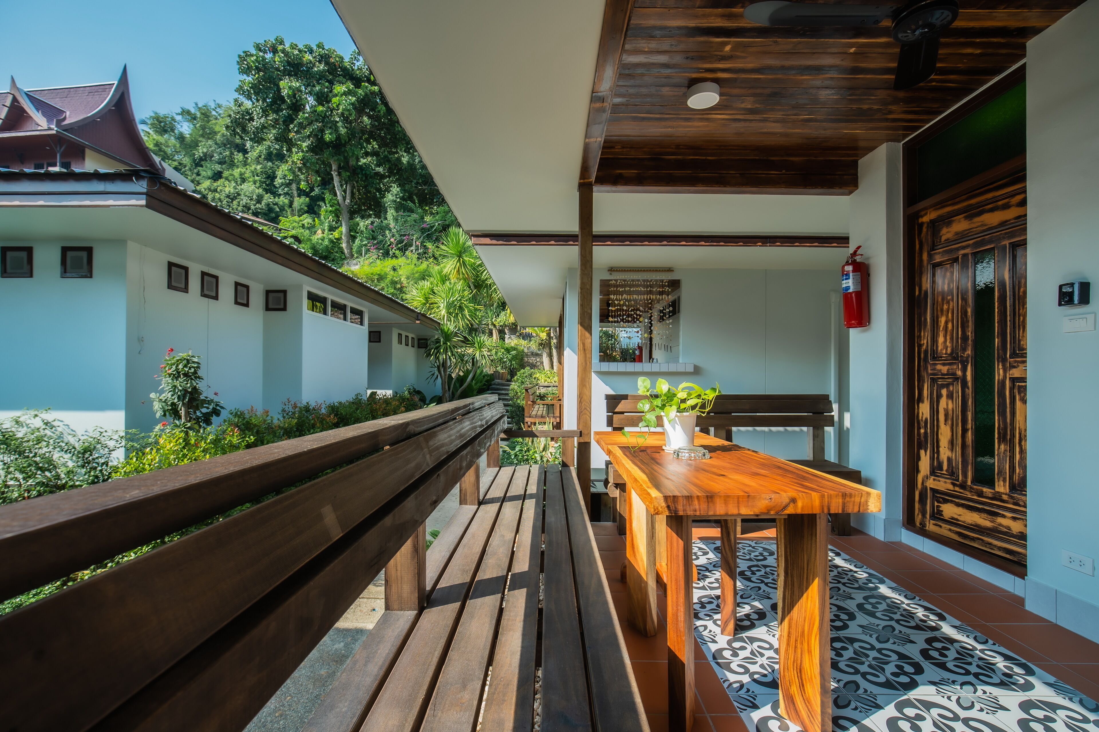 A wooden bench and table on a balcony with a view of a traditional building and greenery.