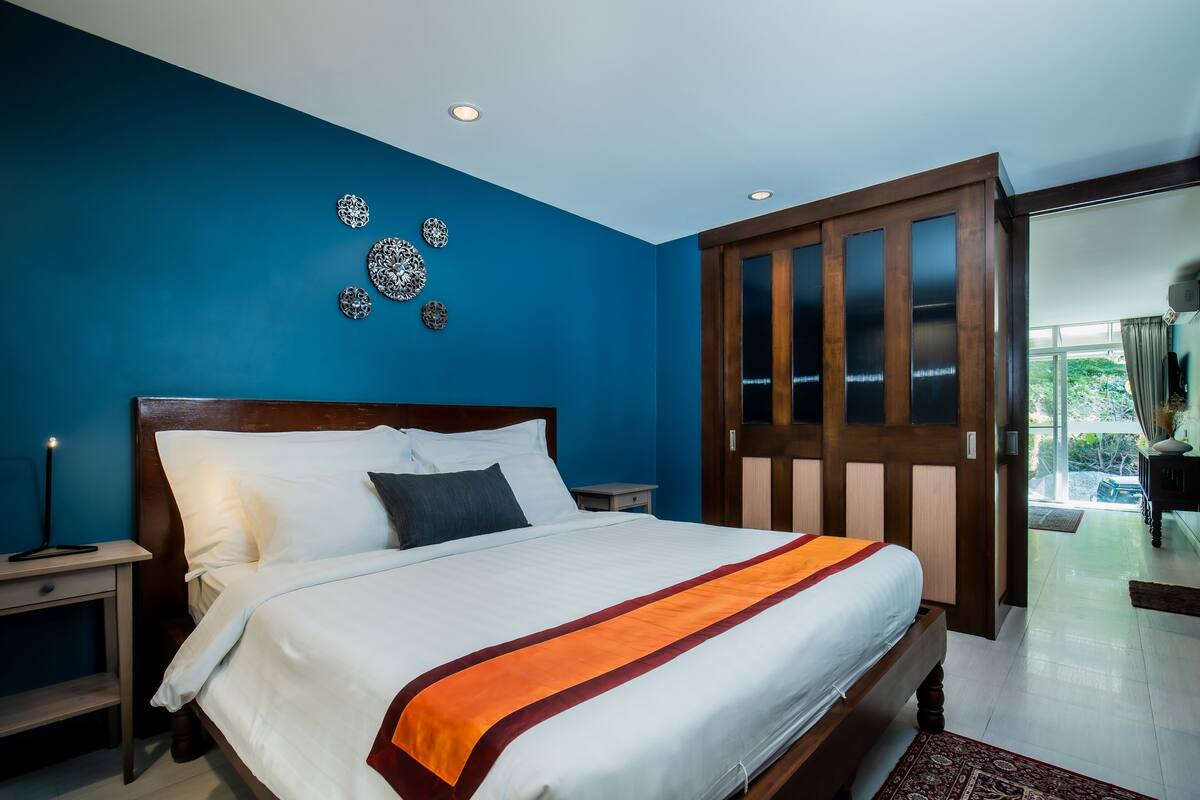 Habitación de hotel con una cama grande, cabecera de madera, mesita de noche y vistas al exterior a través de una puerta corredera.