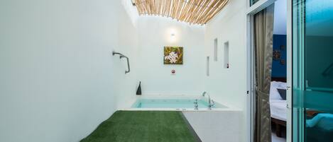 A modern bathroom with a bathtub, a shower area, and a green artificial grass mat.
