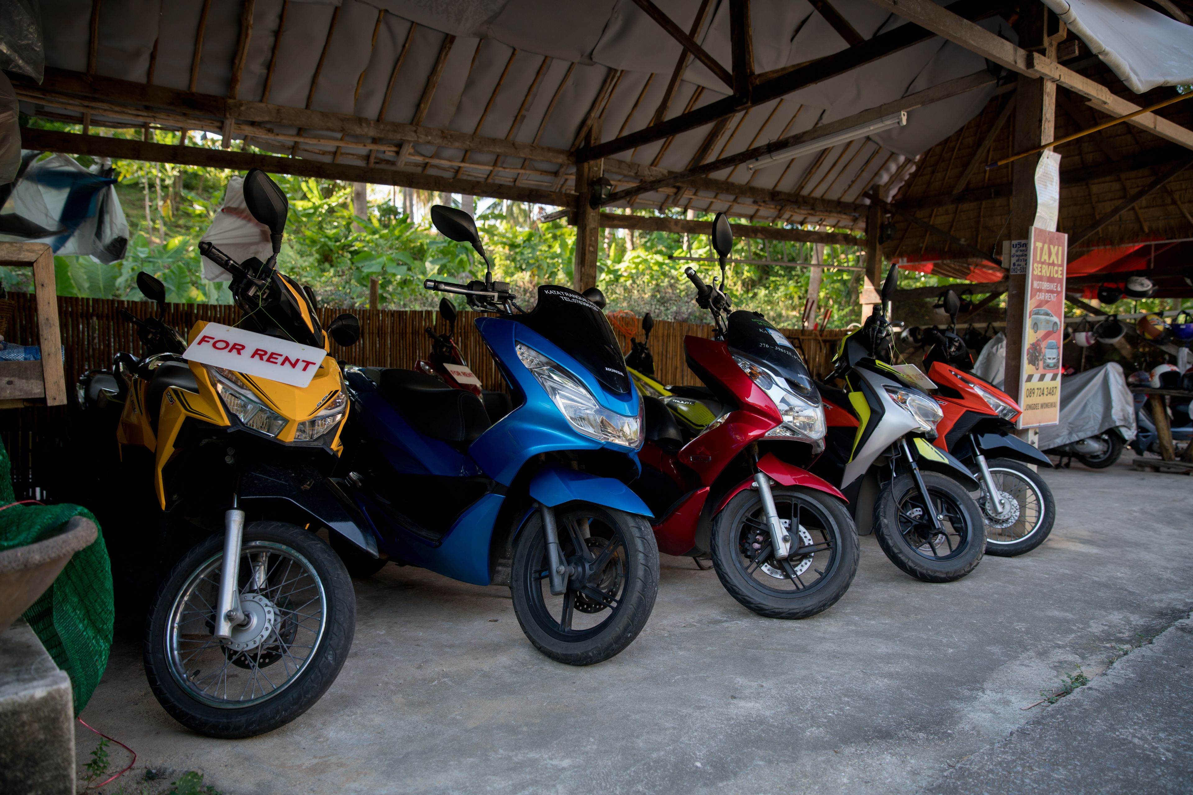 Varias motocicletas estacionadas bajo un refugio, con un cartel que indica disponibilidad de alquiler.
