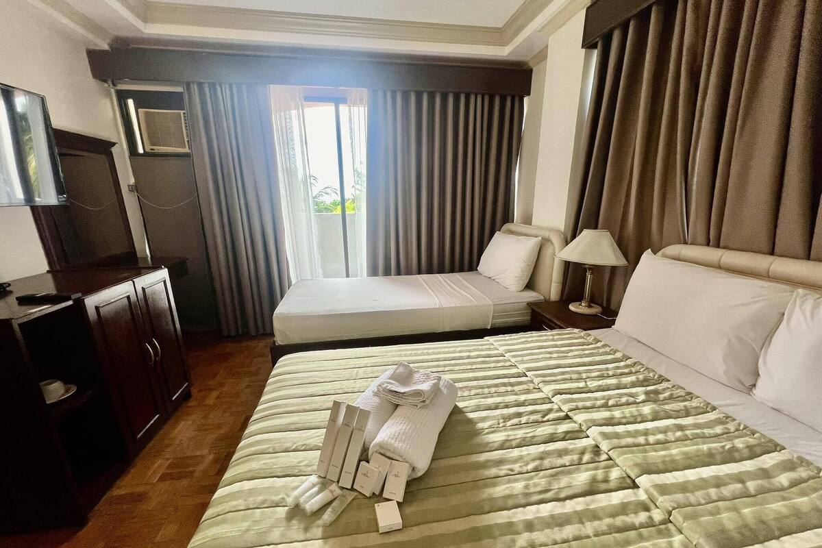 A hotel room with a large bed, a desk, a chair, a TV, and a window with curtains.