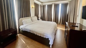 A hotel room with a large bed, a dresser, a TV, and curtains.