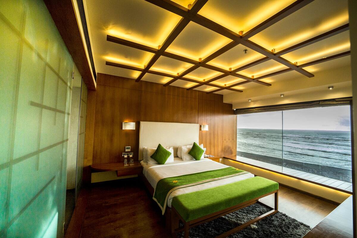 Een moderne slaapkamer met een groot bed, houten lambrisering, uitzicht op zee en een uniek plafondontwerp.