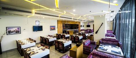 Un ristorante con diversi tavoli e banconi, un'area bar e un'ampia finestra con tende.