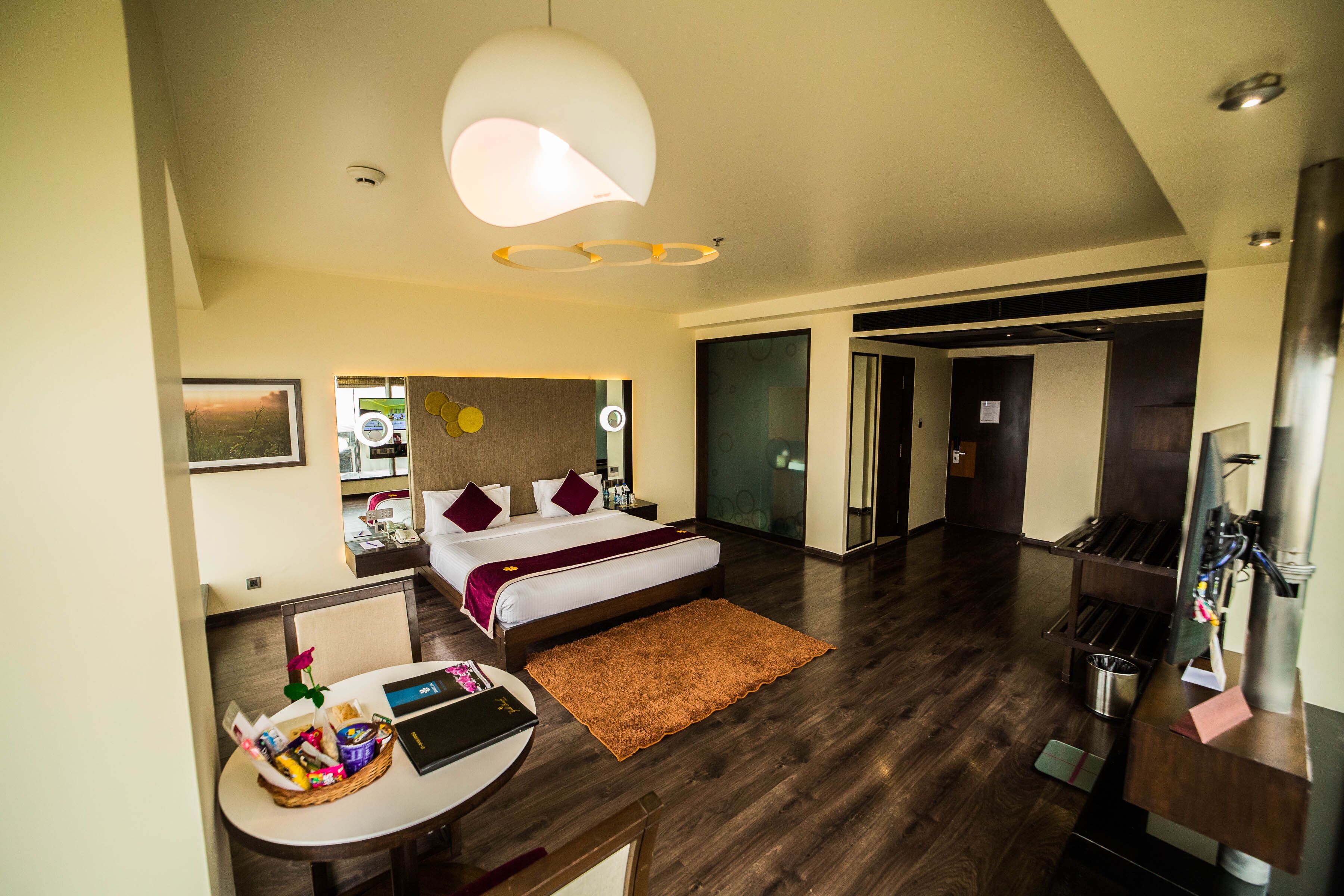 A modern hotel room with a bed, a desk with a laptop, a coffee machine, and a breakfast bar.