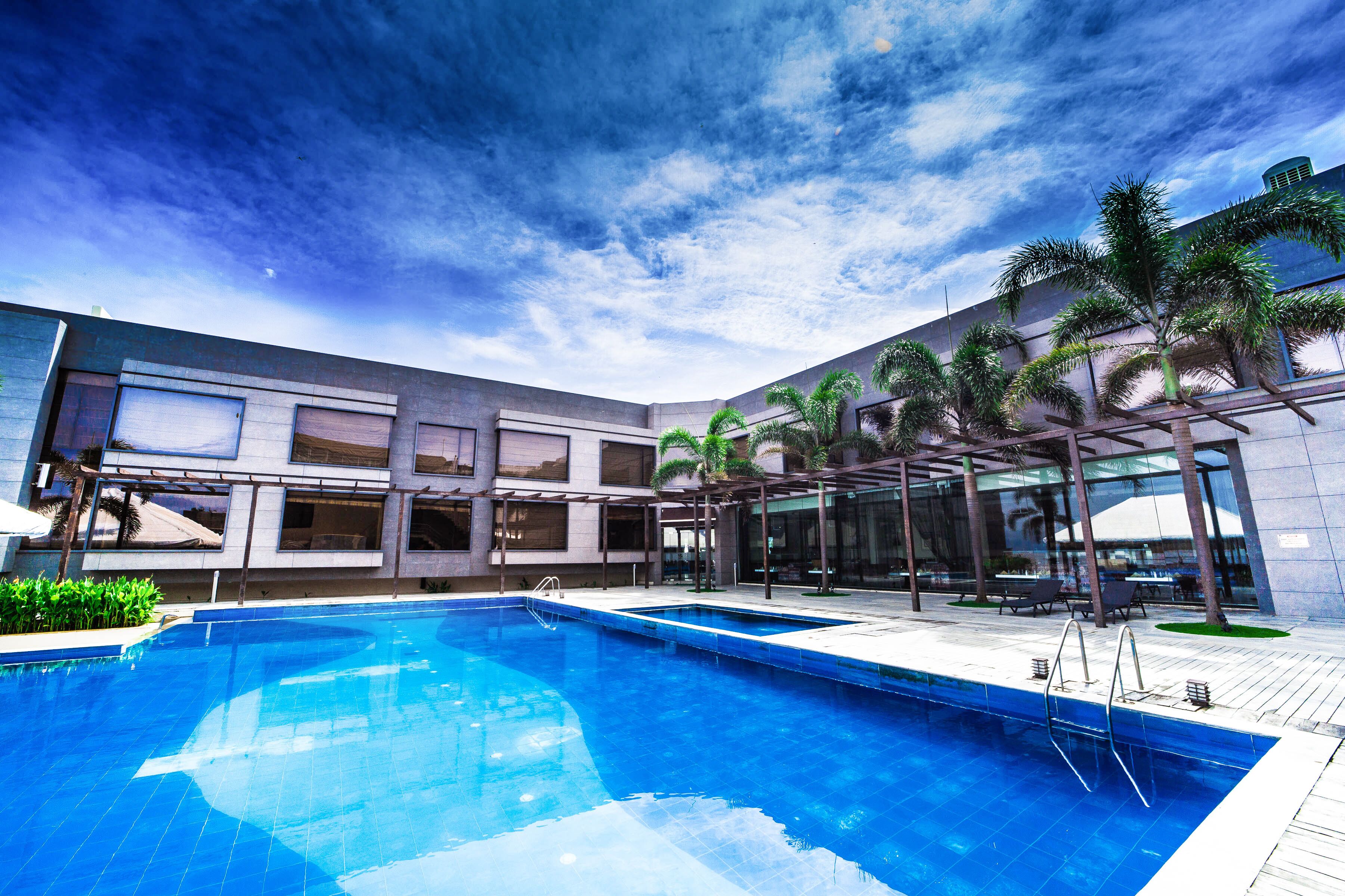 A modern hotel with a swimming pool, outdoor seating, and palm trees.