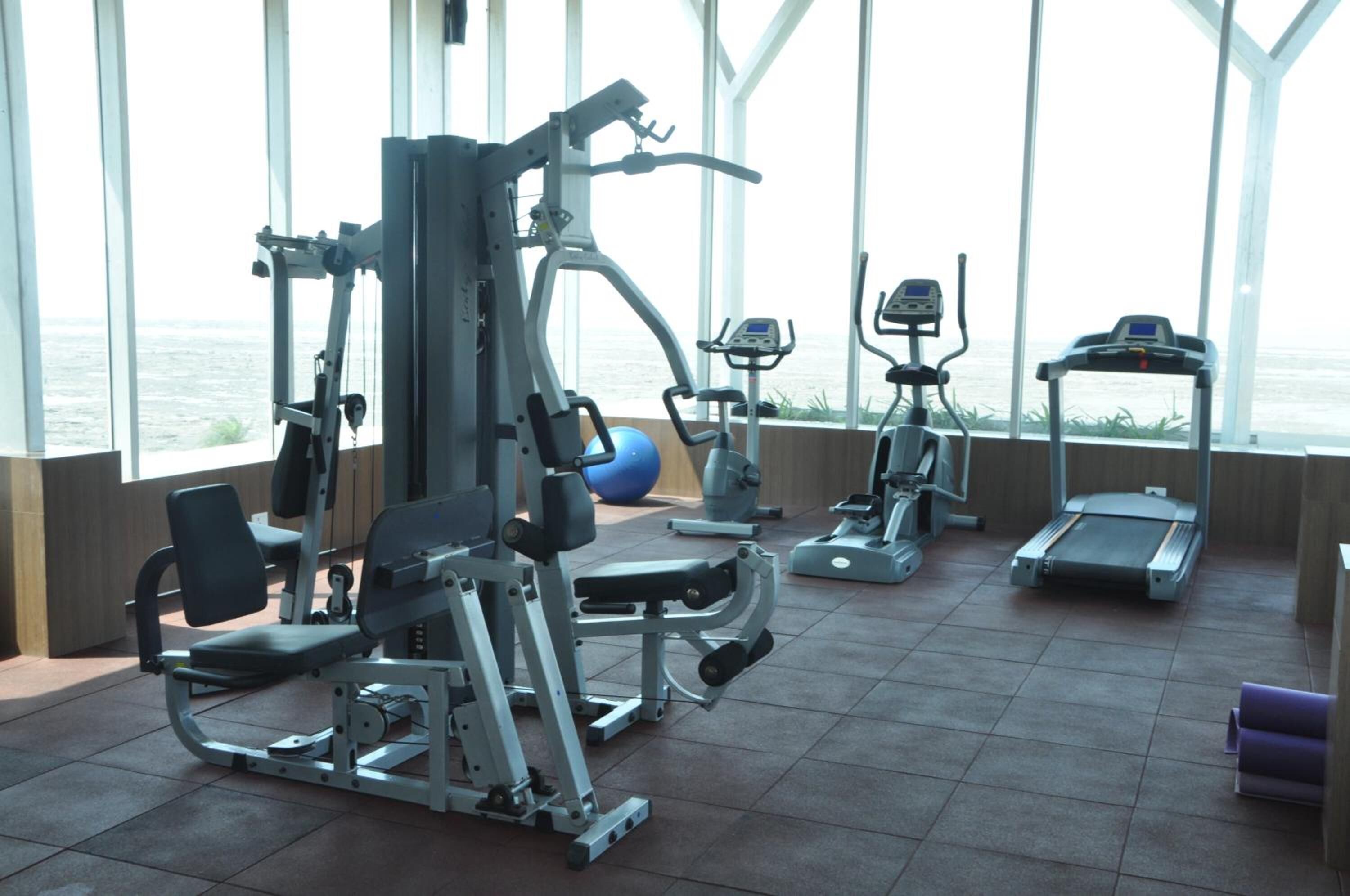 Ett gym med olika typer av träningsutrustning, stora fönster och utsikt över havet.
