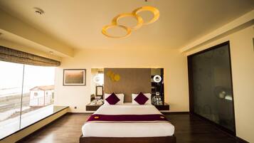 A modern hotel room with a large bed, a view through a window, and a unique circular light fixture above the bed.