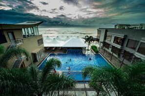 A swimming pool with a view of the ocean, surrounded by palm trees and modern architecture. - The Gold Beach Resort (Daman)