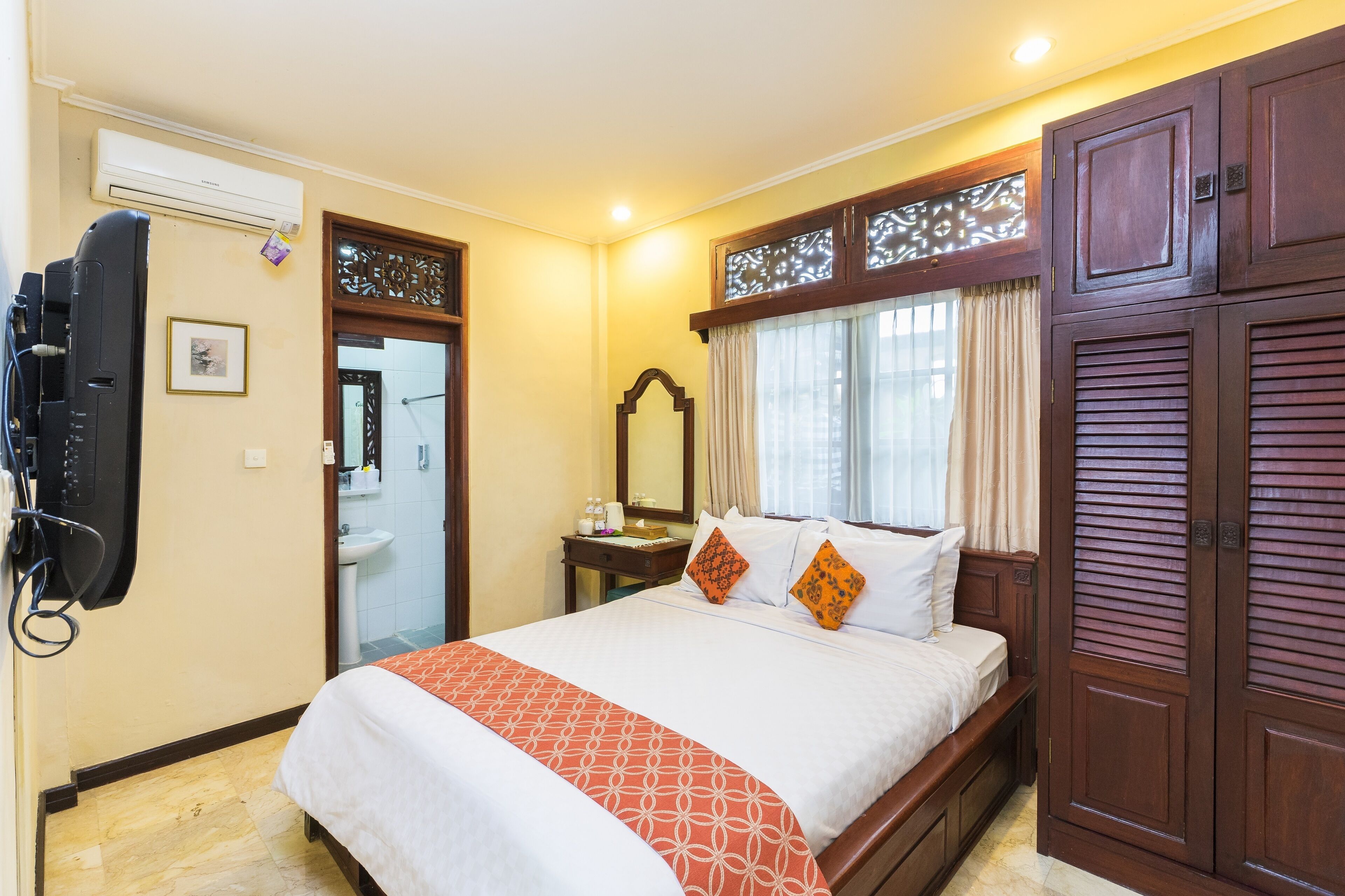 A hotel room with a bed, a bedside table, a mirror, a wardrobe, and an air conditioning unit.