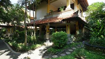 A two-story building with a balcony, surrounded by lush greenery and a stone pathway.