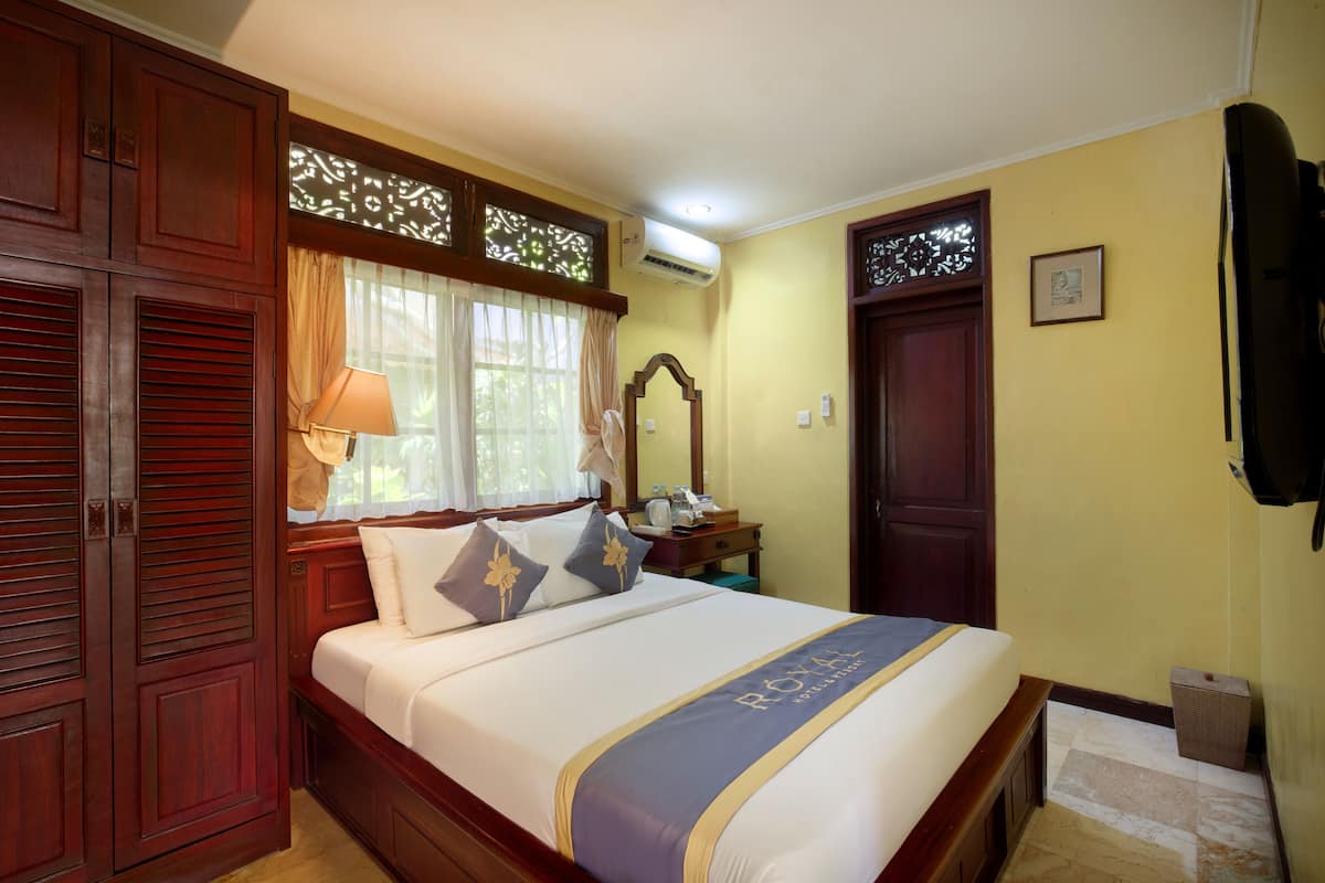 A hotel room with a bed, wooden wardrobe, a nightstand, a mirror, and a window with curtains.