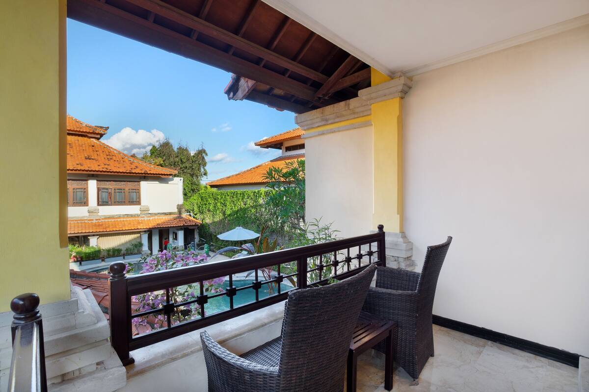 A balcony with wicker chairs, a pool, and a view of traditional buildings.