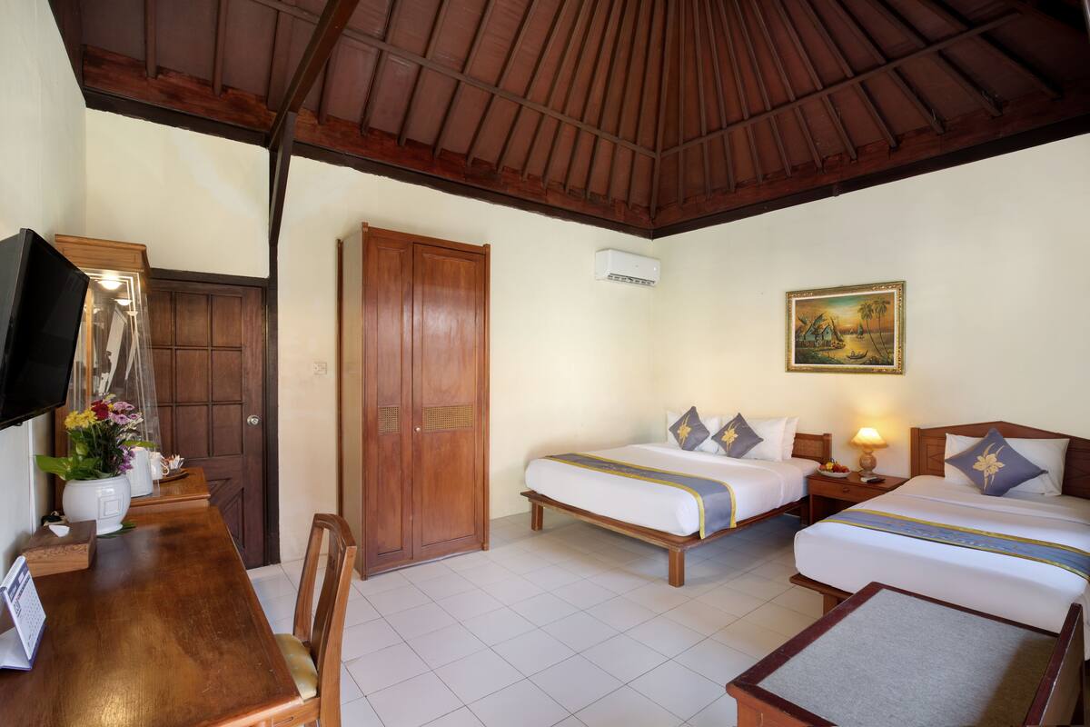 A hotel room with two beds, a wooden ceiling, a dining table with chairs, a TV, and a painting on the wall.
