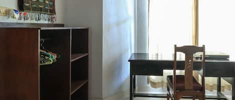 Una habitación con escritorio de madera, una silla, estantería y ventana con cortina.