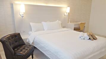 Une chambre d’hôtel avec un lit soigneusement fait, un fauteuil en cuir, un bureau avec une chaise et une serviette pliée posée sur le lit.