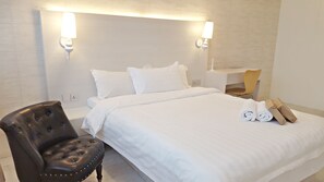 A hotel room with a neatly made bed, a leather armchair, a desk with a chair, and a rolled towel on the bed. - Creator Hotel (Kulai)
