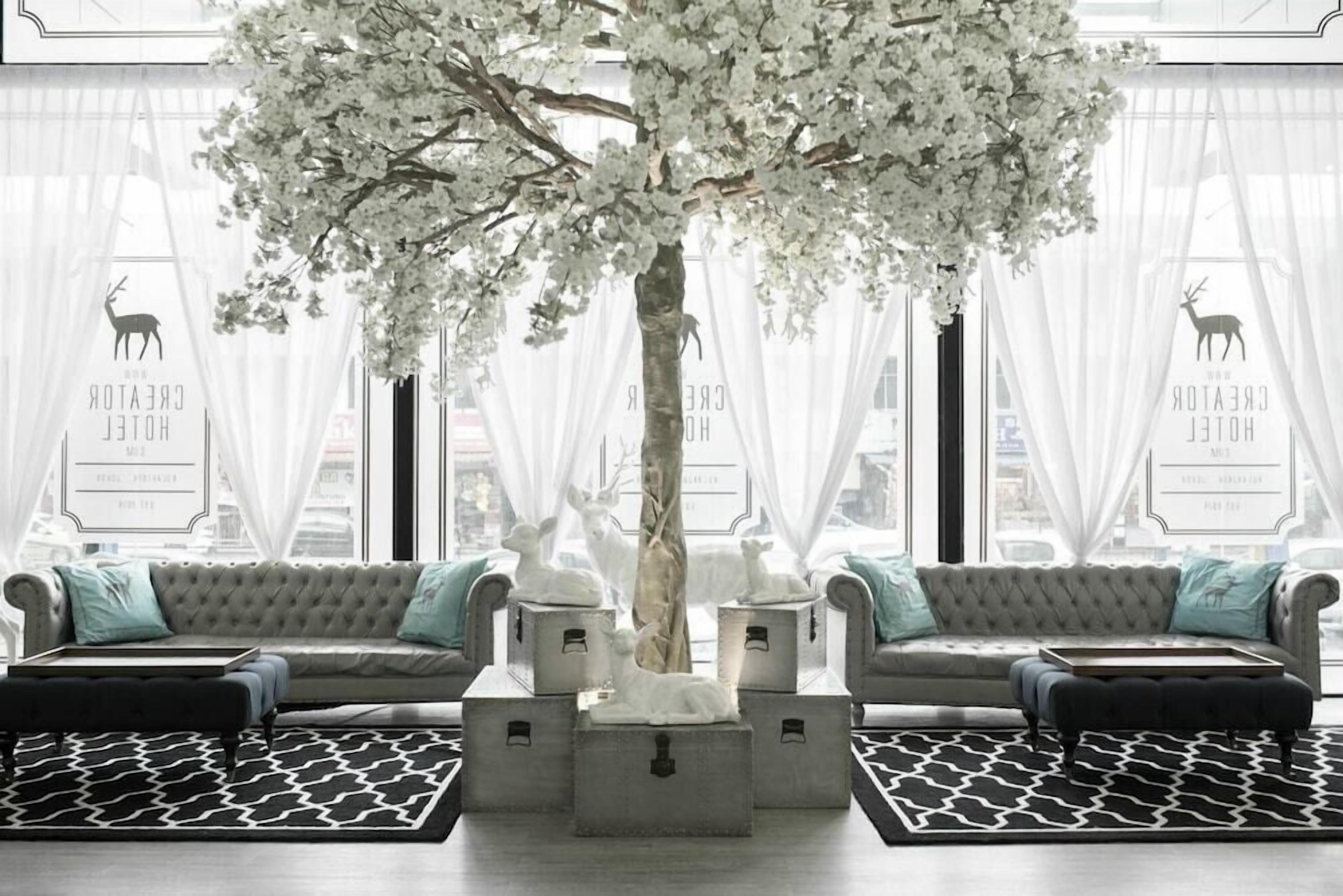A modern hotel lobby with a large tree, two sofas, and a patterned rug.