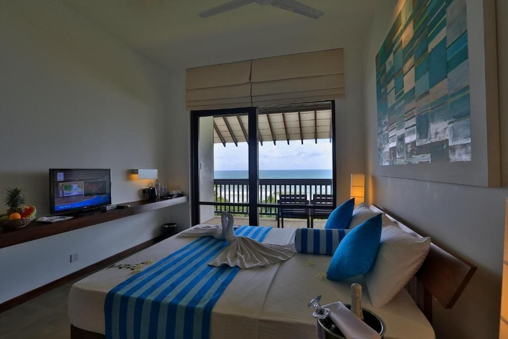 Habitación de hotel con cama, televisión, balcón con vistas y un cuadro en la pared.
